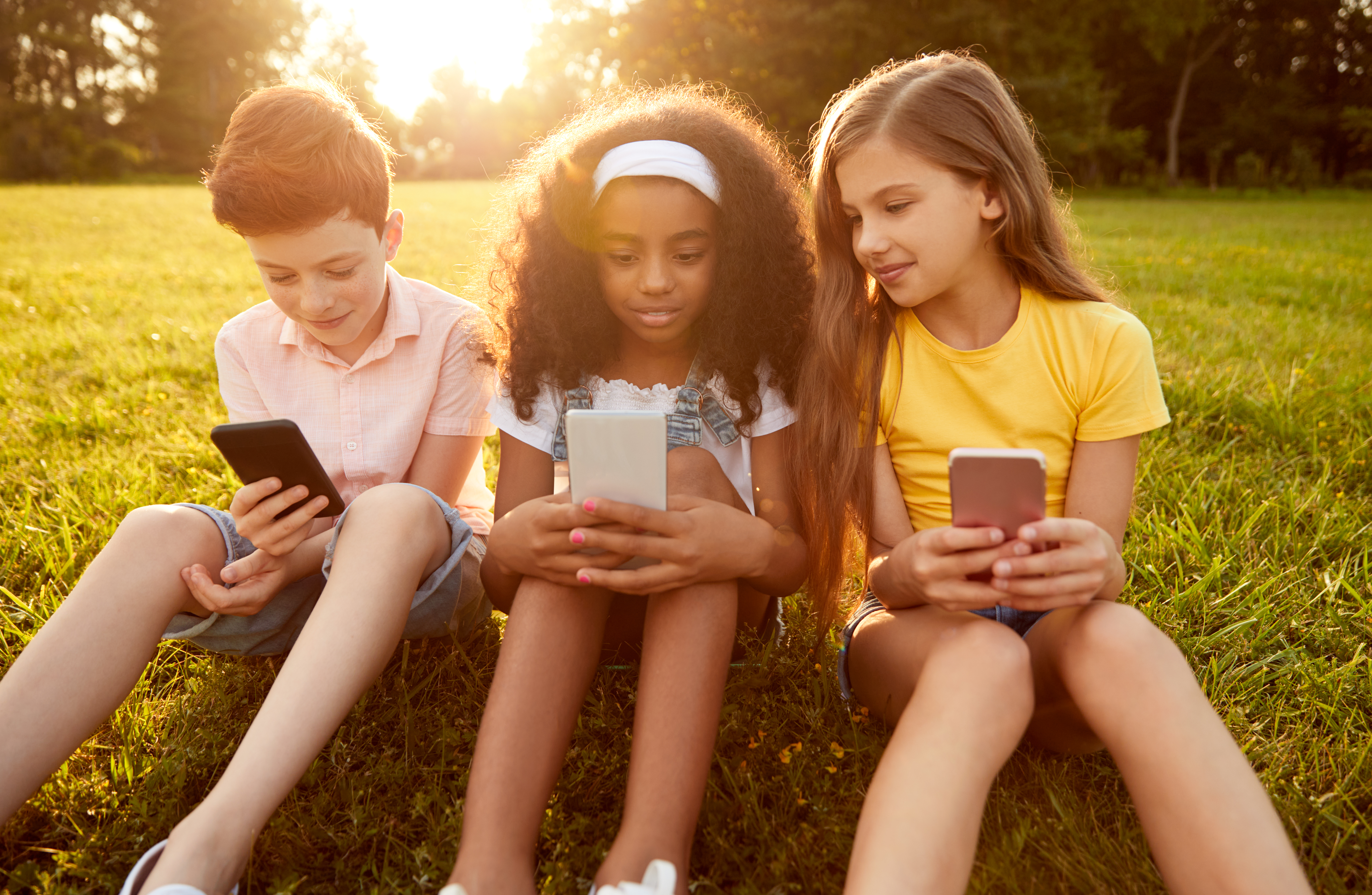 Diverse kids browsing smartphones in park